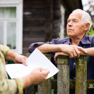 Een oudere man praat met een buurman bij het hek van zijn huis in de wijk.